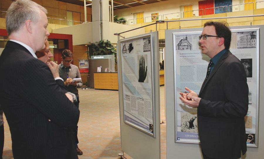 Universitätsarchivar Dr. Marcus Holtz führt in der Sparkasse Mainfranken durch die Ausstellung "120 Jahre Röntgenstrahlen". Links Bernd Fröhlich, Vorstandsvorsitzender der Sparkasse. (Foto: Reinhold Bürkner)